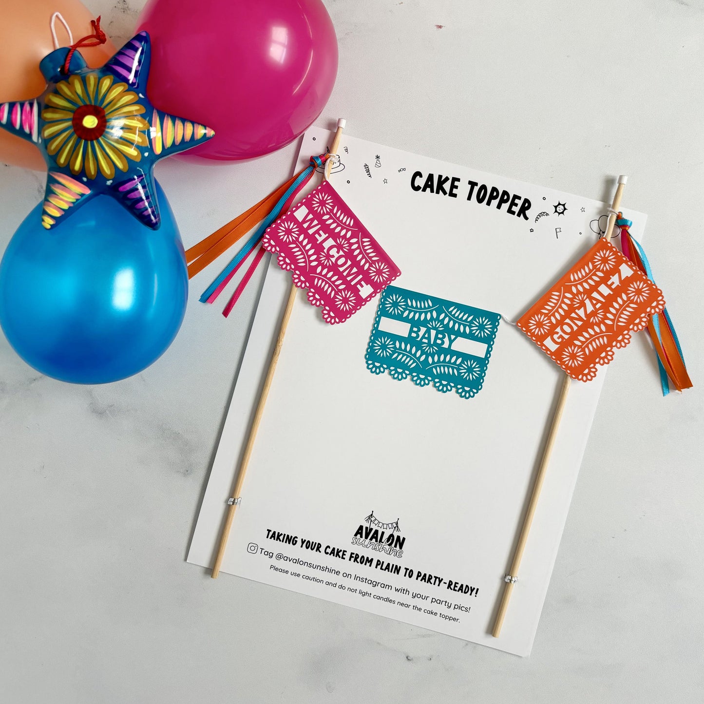 Fiesta theme baby shower cake topper with 3 papel picado style flags on a cake banner in bright pink, aqua and orange.  Wording says WELCOME BABY NAME | personalized cake toppers by Avalon Sunshine