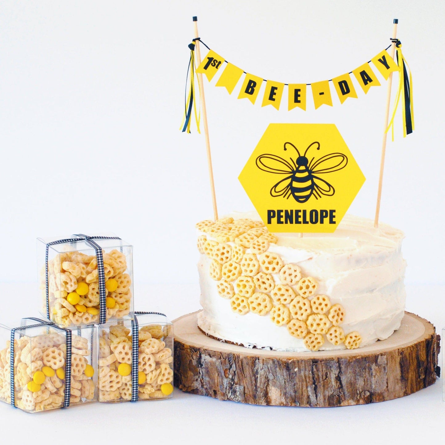 1st bee day cake banner with yellow hexagon shaped cake topper.  Topper has a black bee image personalized with name.  Shown with honeycomb cereal party favors