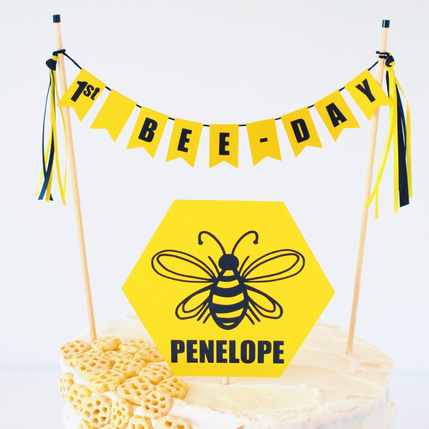 1st bee day cake banner with yellow hexagon shaped cake topper.  Topper has a black bee image personalized with name