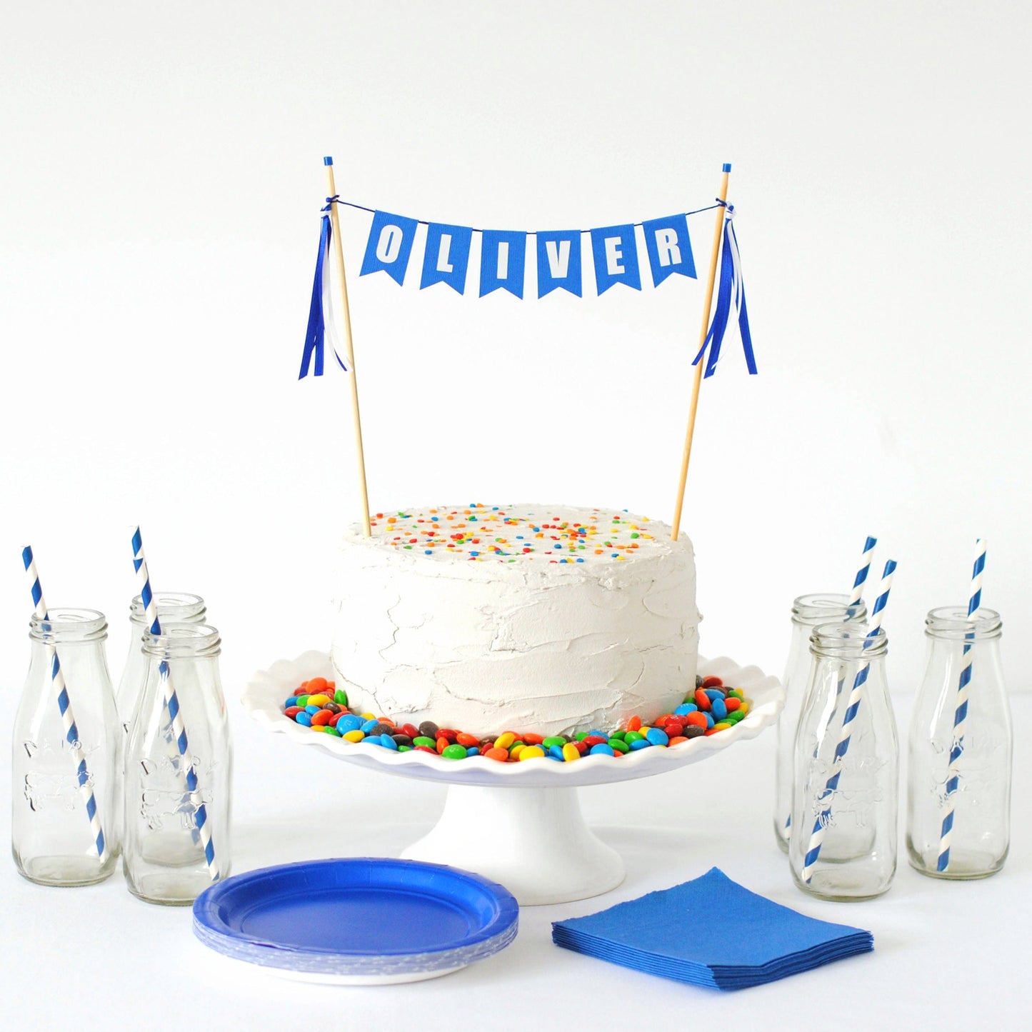 royal blue name cake topper shown on a white cake with colorful sprinkles