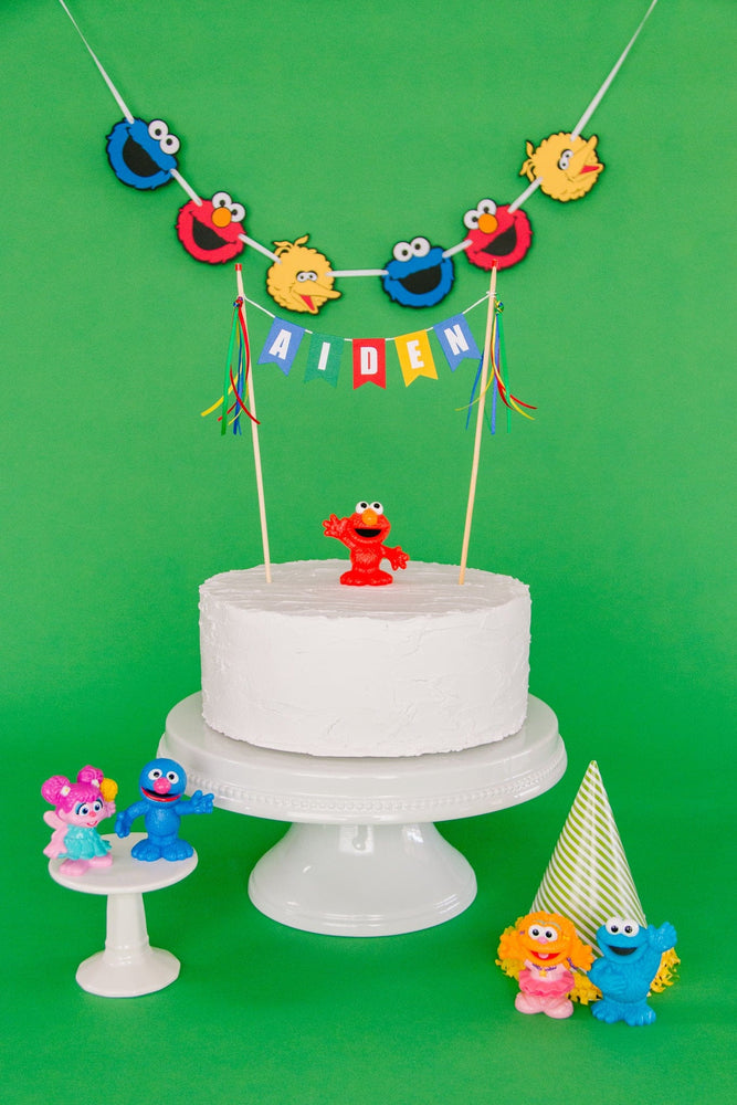 
                  
                    personalized name cake topper in blue, green, red and yellow. Styled with Sesame Street party decorations
                  
                