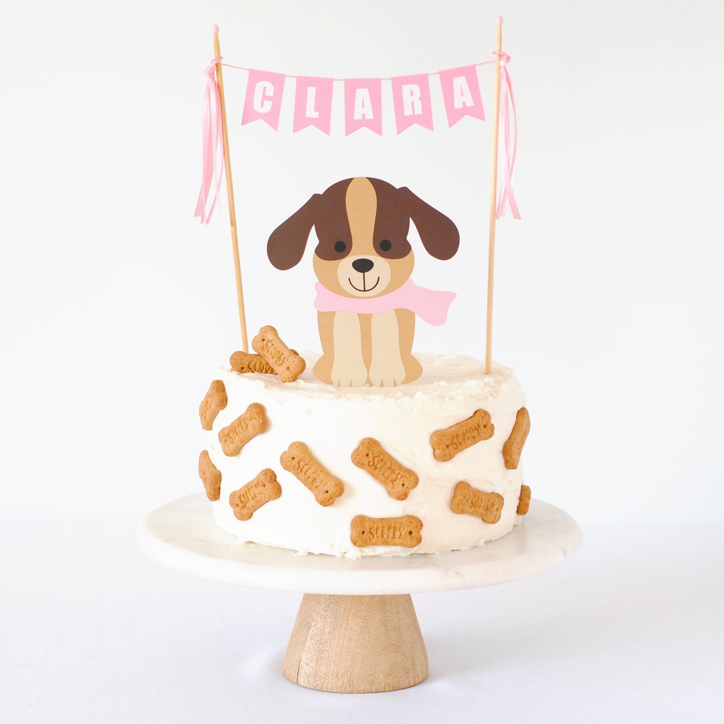 puppy theme cake topper set with brown puppy wearing a pink scarf and pink name banner on a white cake decorated with scooby snack cookies