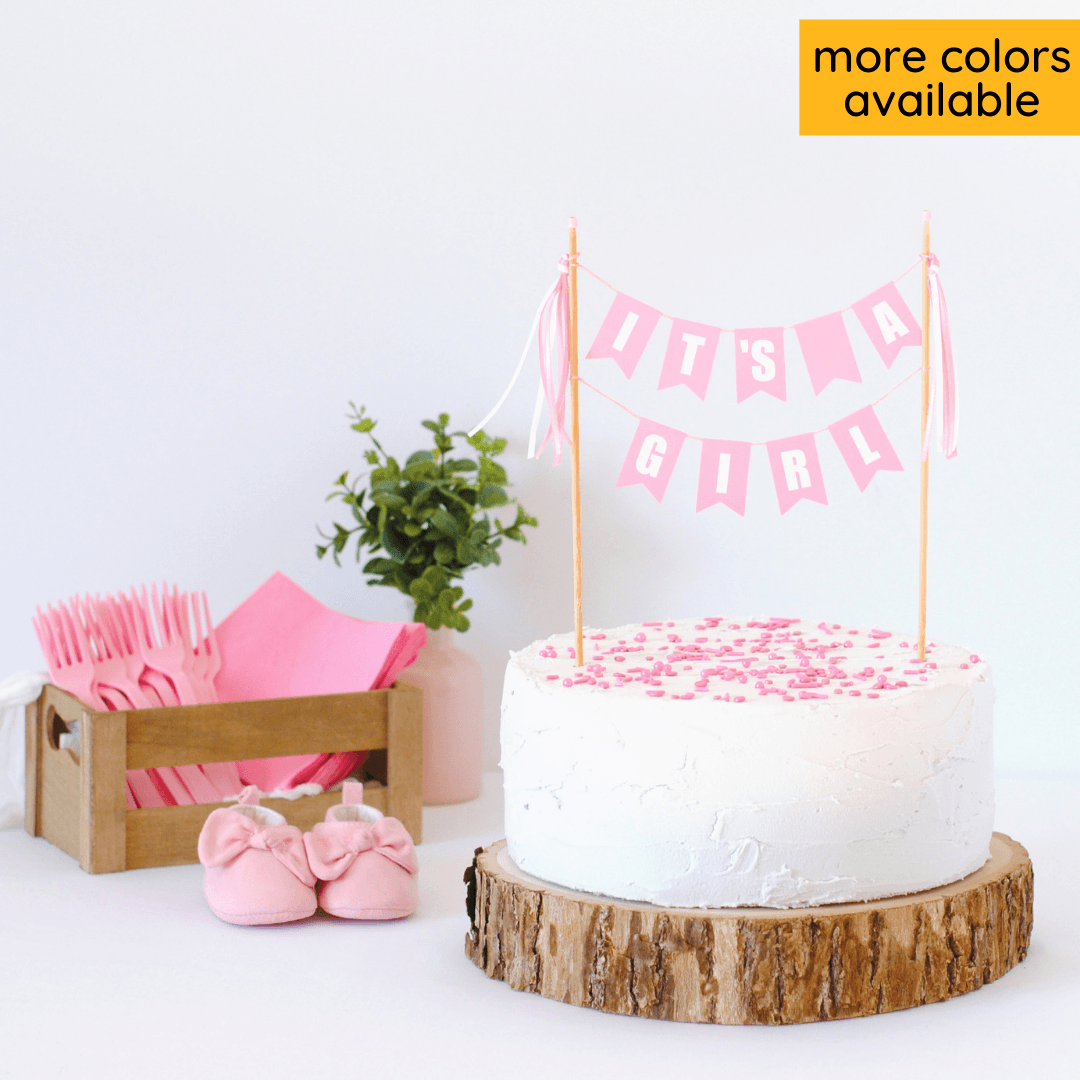 pastel pink two-tier cake topper with text "it's a girl" shown on a white cake