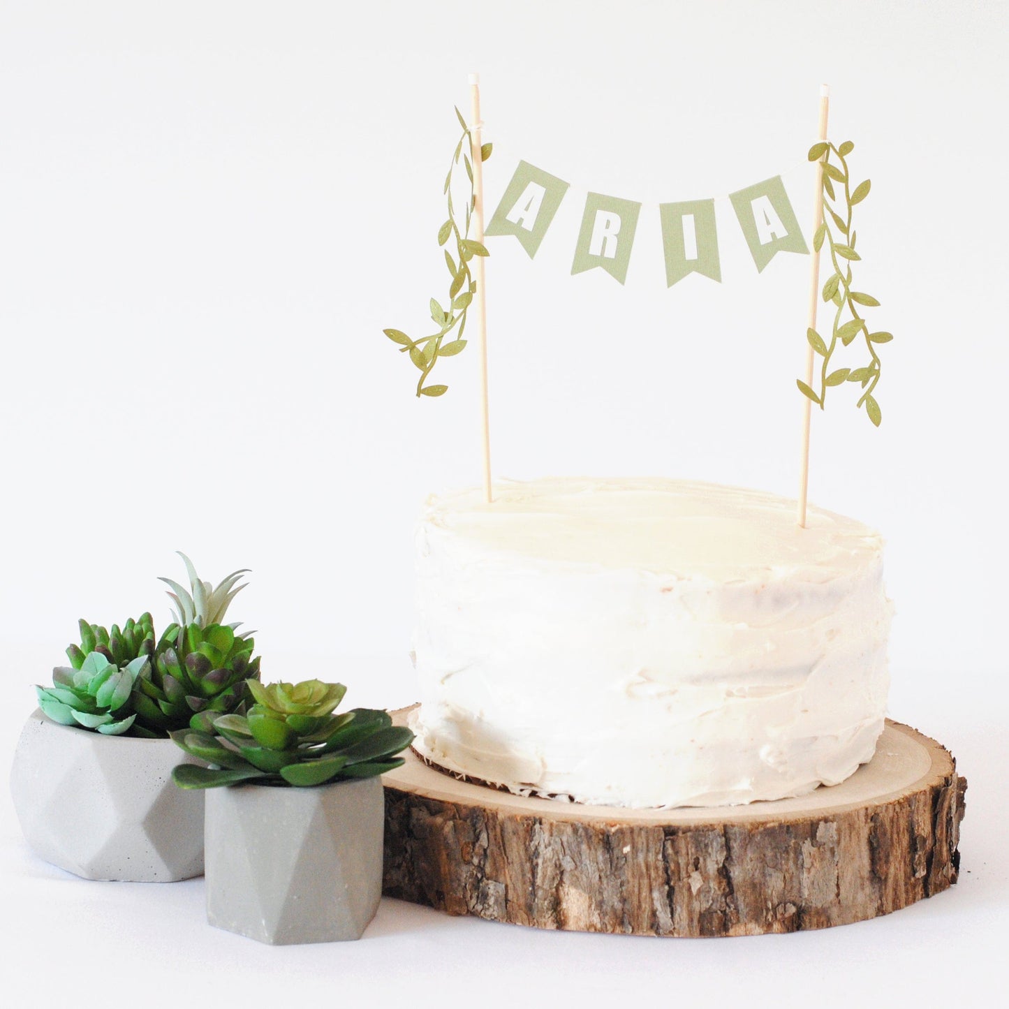 Greenery themed personalized cake topper shown on a white cake with succulents