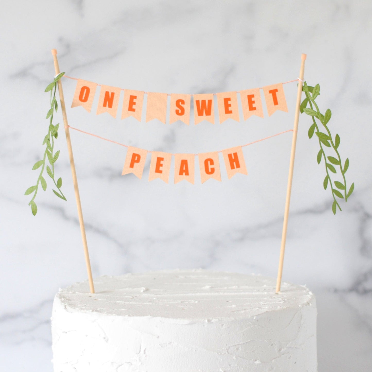 Two tier cake topper banner with wording ONE SWEET PEACH in peach color with orange letters and leafy ribbons on the ends