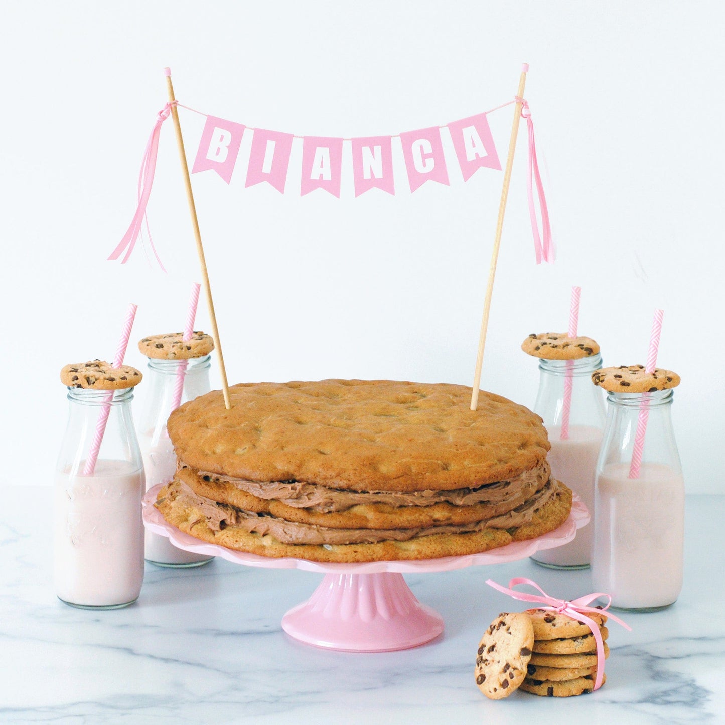 pastel pink birthday cake topper for girls, name banner shown on a layered chocolate chip cookie cake