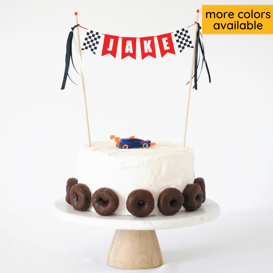 race car party cake topper personalized with name and checkered flags shown on a cake with chocolate donut tire decorations