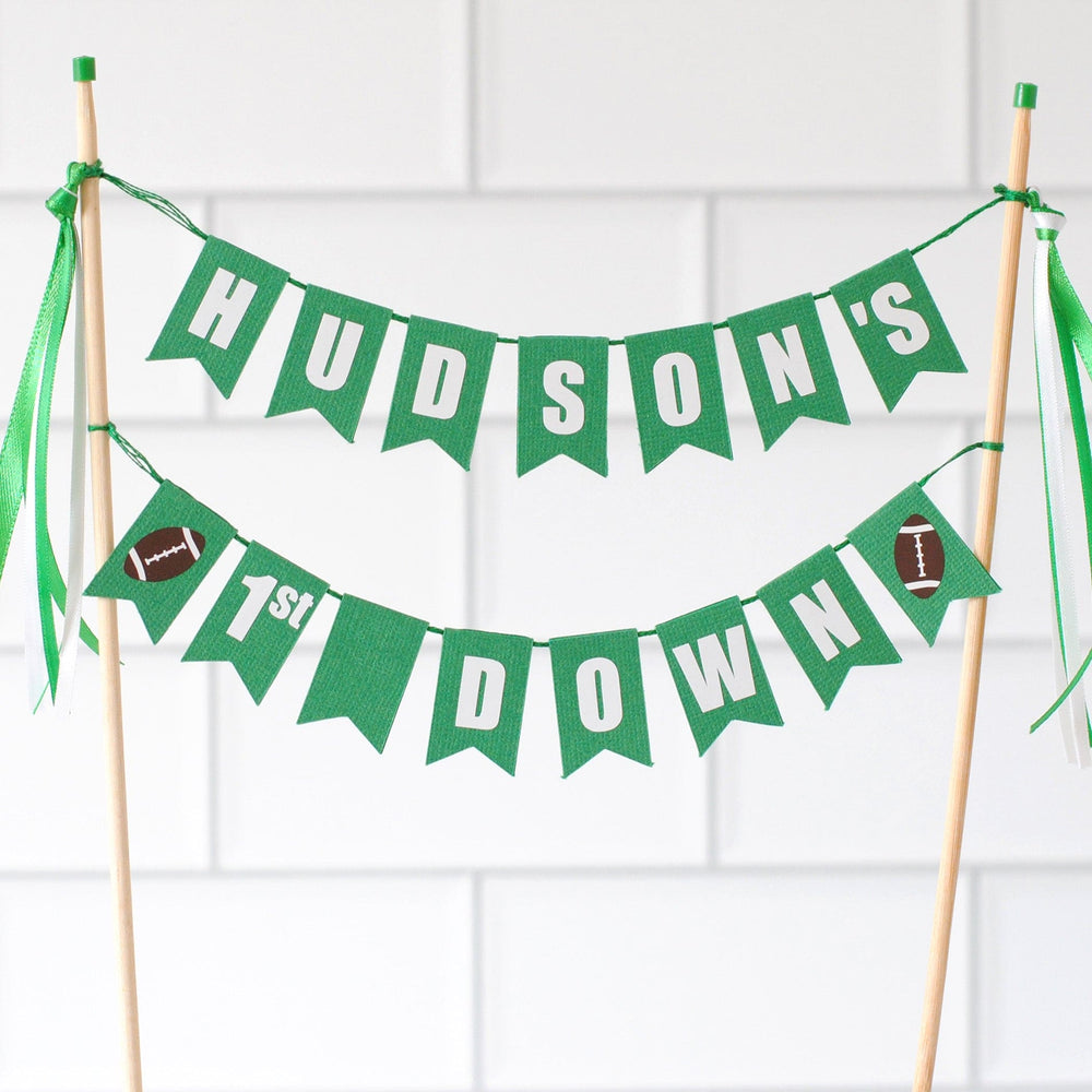 
                  
                    Green birthday banner with 'Hudson's 1st Down' on a white tiled wall background | personalized cake toppers by Avalon Sunshine
                  
                