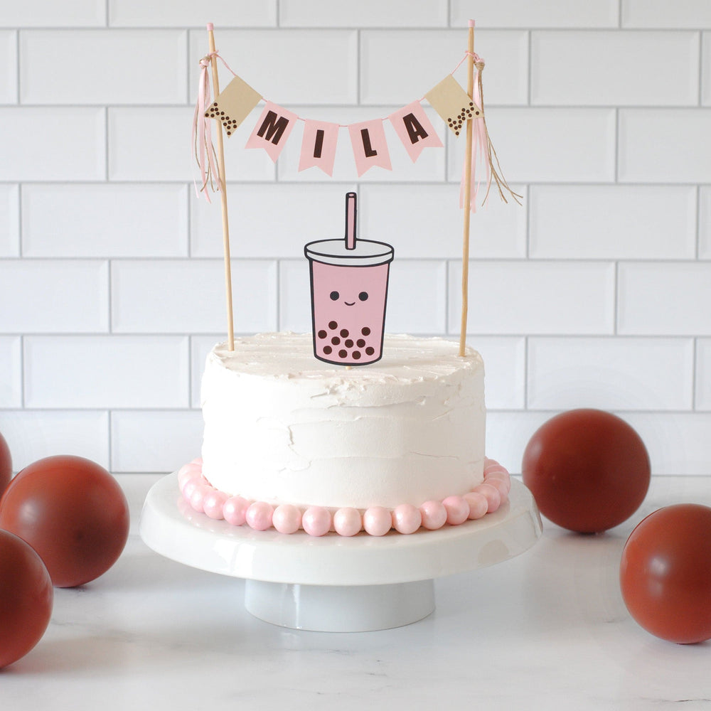 White cake with pink decorations and a 'Mila' banner on a white background.  Under the name is a Pink Boba Drink topper