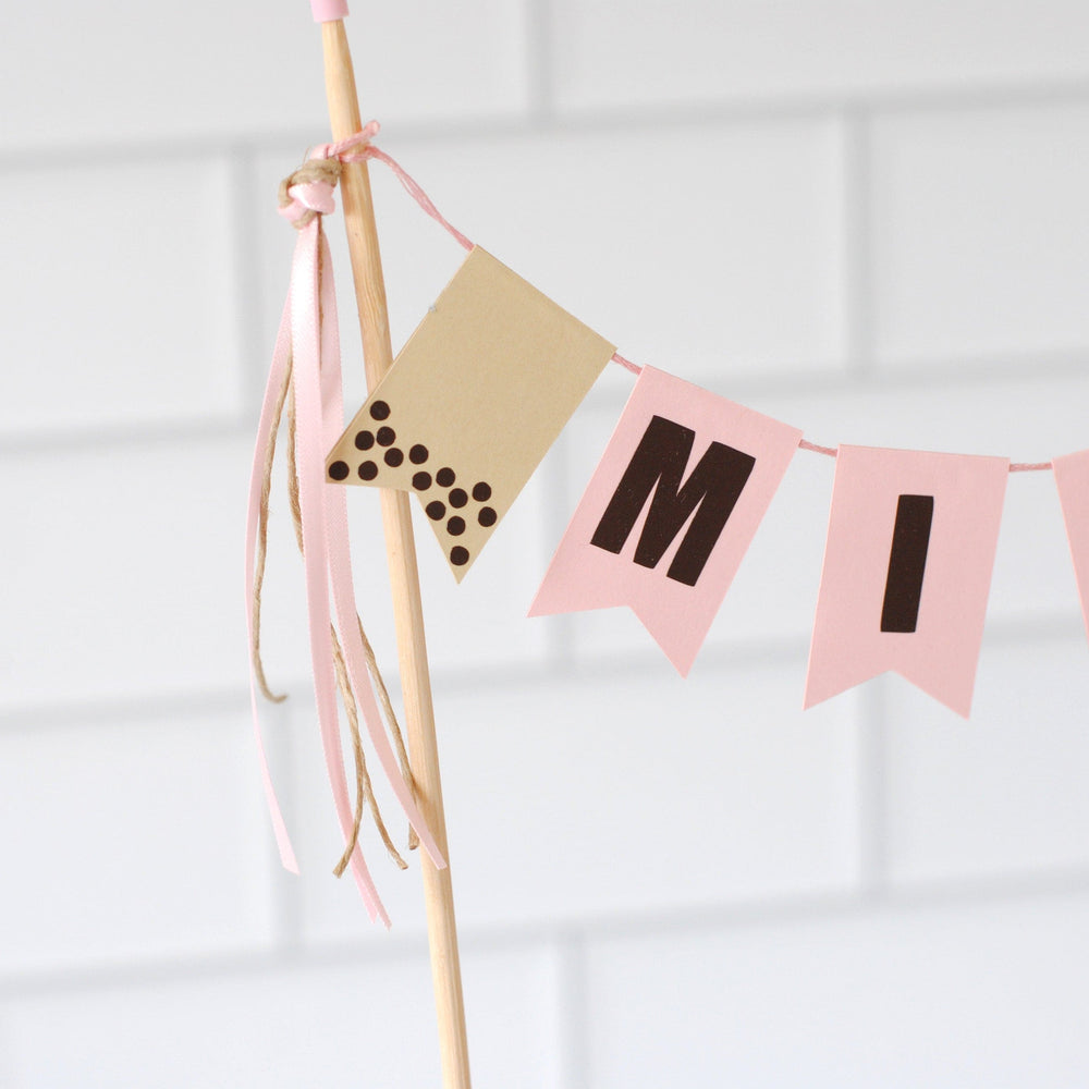
                  
                    Close up view of cake topper banner for a Boba theme. Personalized flags with name and a beige flag with dark brown dots to look like boba
                  
                