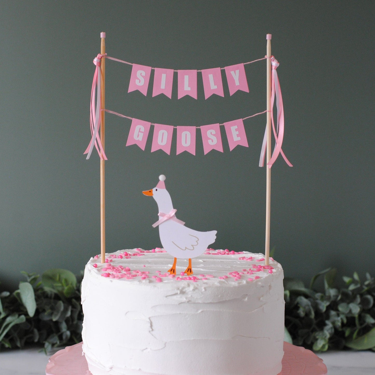 
                  
                    White cake with a goose topper and pink 'Sally Goose' banner on a dark background | cake topper by Avalon Sunshine

                  
                