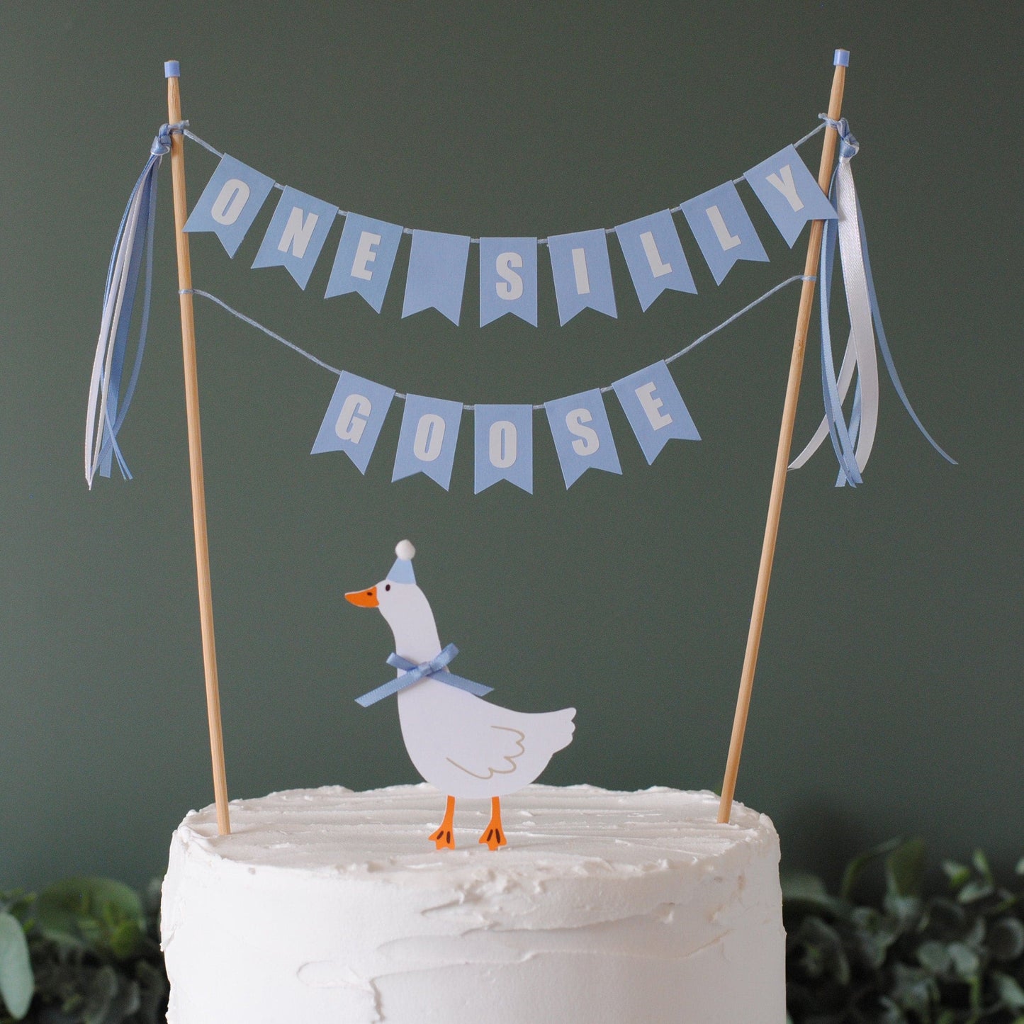 
                  
                    Cake with a goose topper and 'One Silly Goose' banner on a dark background | cake topper by Avalon Sunshine
                  
                