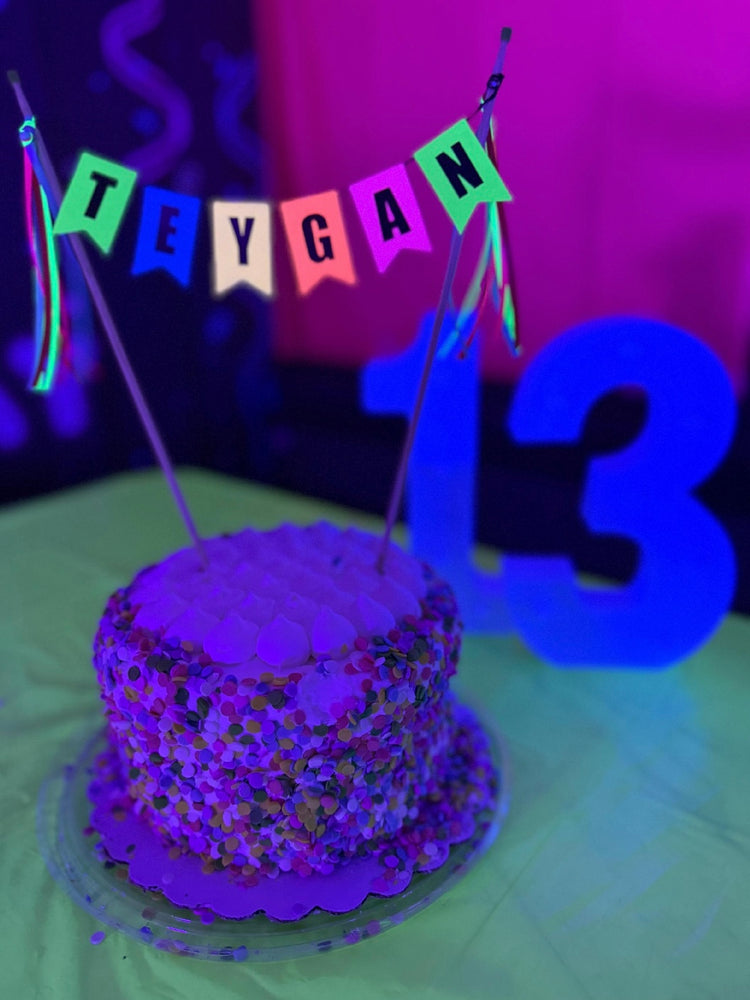 
                  
                    Neon colored cake topper with name displayed on a small cake with sprinkles under a black light to make the colors “glow” | personalized cake toppers by Avalon Sunshine
                  
                