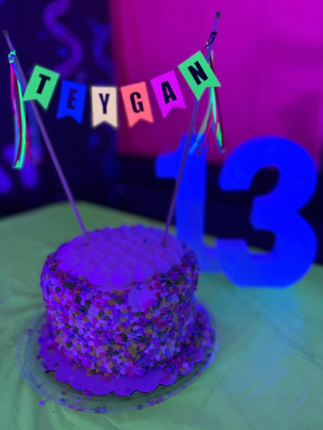 
                  
                    Neon colored cake topper with name displayed on a small cake with sprinkles under a black light to make the colors “glow” | personalized cake toppers by Avalon Sunshine
                  
                