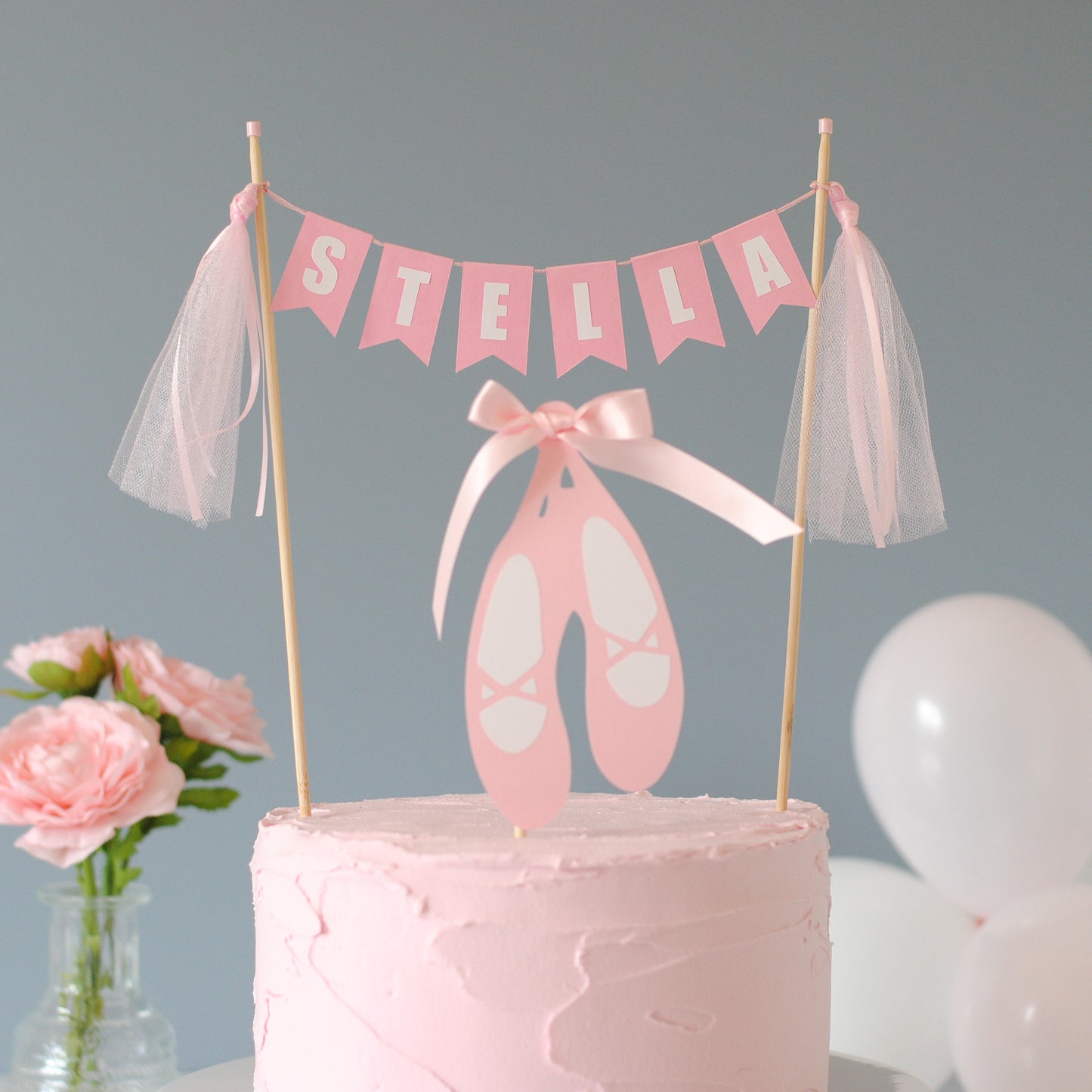 
                  
                    Pink cake with pink name banner with tulle tassels and ballet slipper topper against a gray background | personalized cake toppers by Avalon Sunshine
                  
                