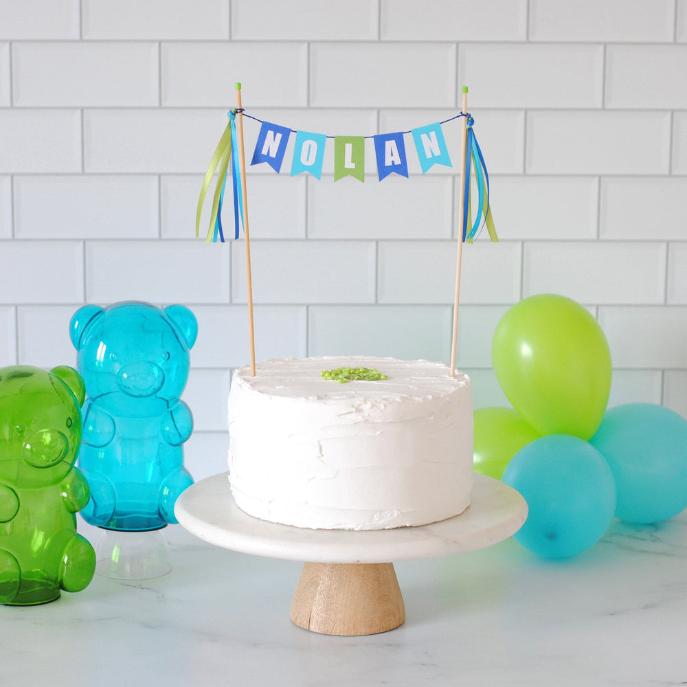 blue turquoise and lime green personalized name cake banner for kids birthday cake  shown on a white cake with gummy bear decorations and balloons in the background| personalized cake toppers by Avalon Sunshine