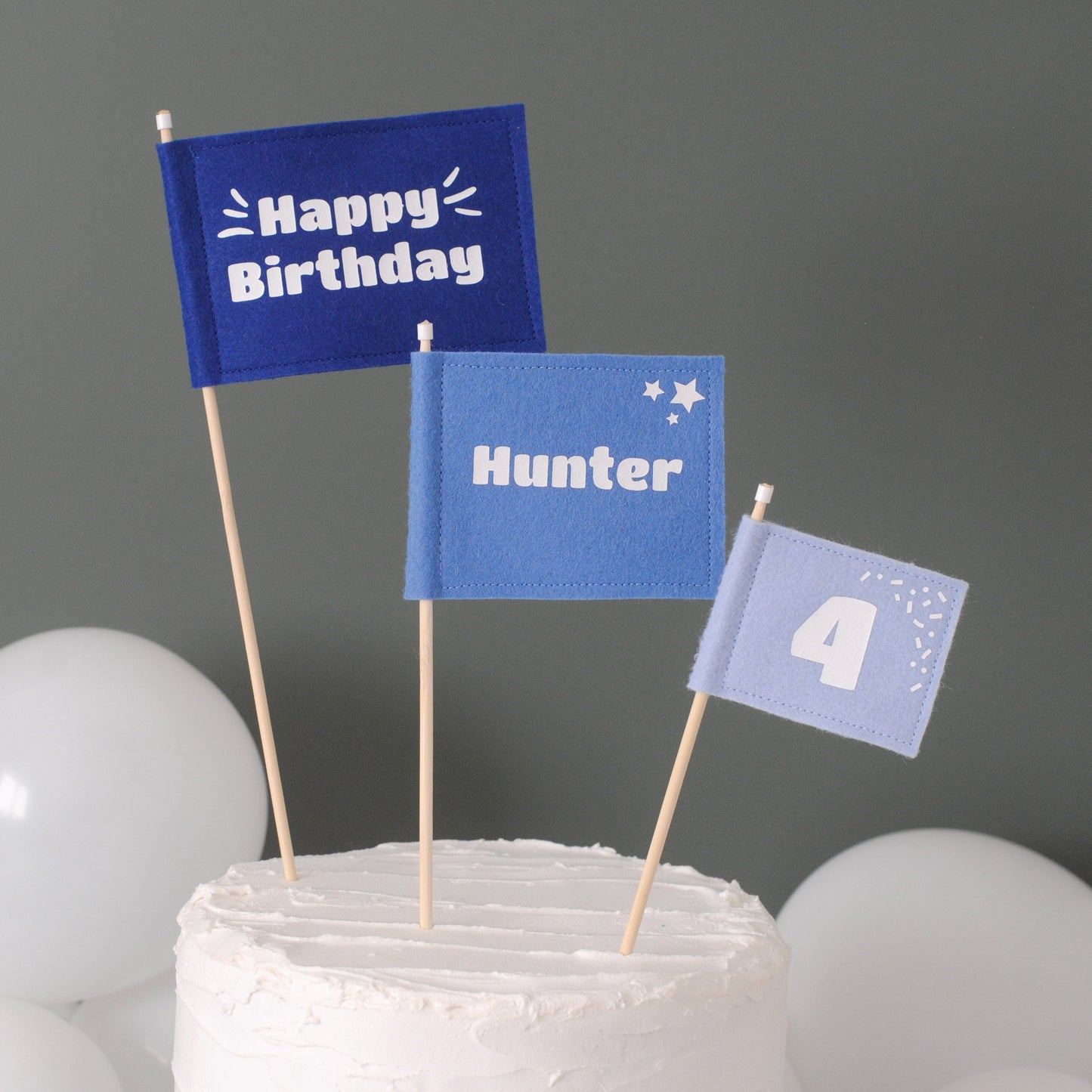 Set of 3 felt flag cake toppers in shades of blue. Large flag with HAPPY BIRTHDAY, medium flag personalized with name HUNTER, and small flag with age 6. 