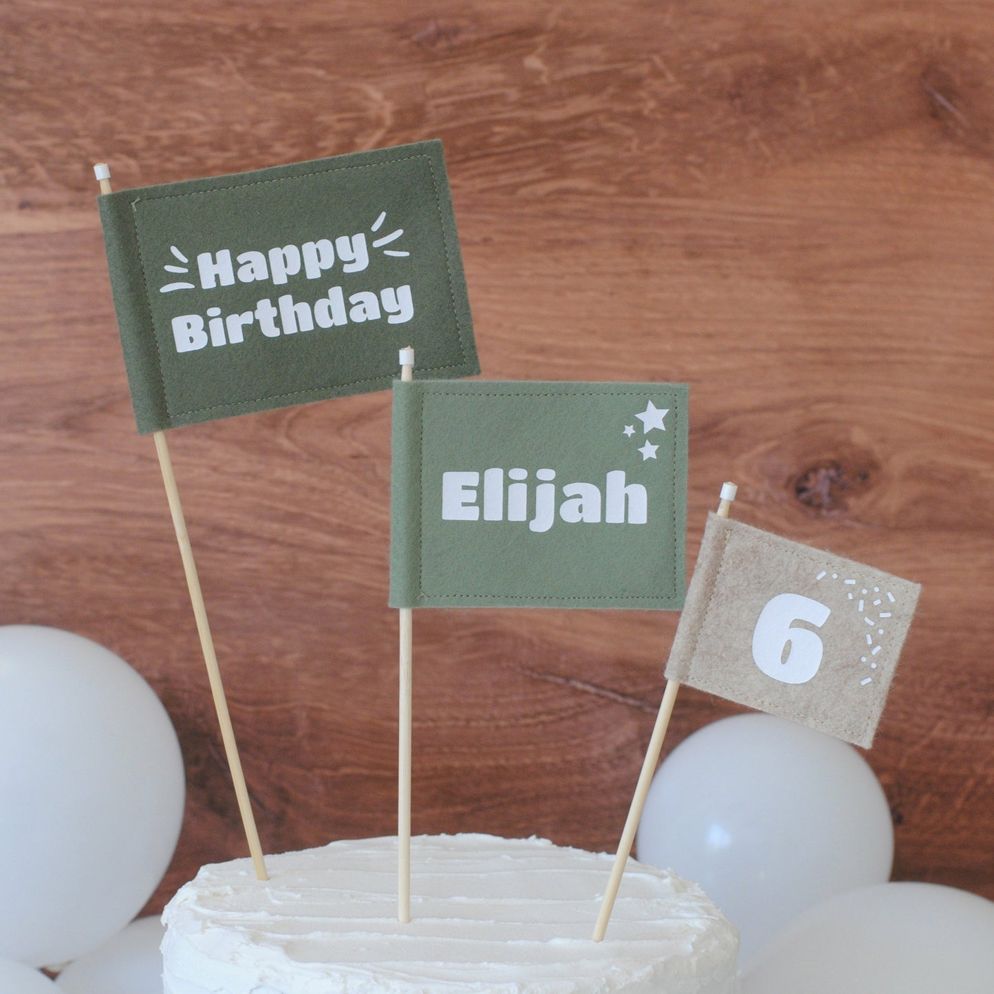 Set of 3 felt flag birthday cake toppers in earthy green and beige colors.  Big flag has HAPPY BIRTHDAY, medium flag is personlized with name ELIJAH, and small flag has age: 6. 