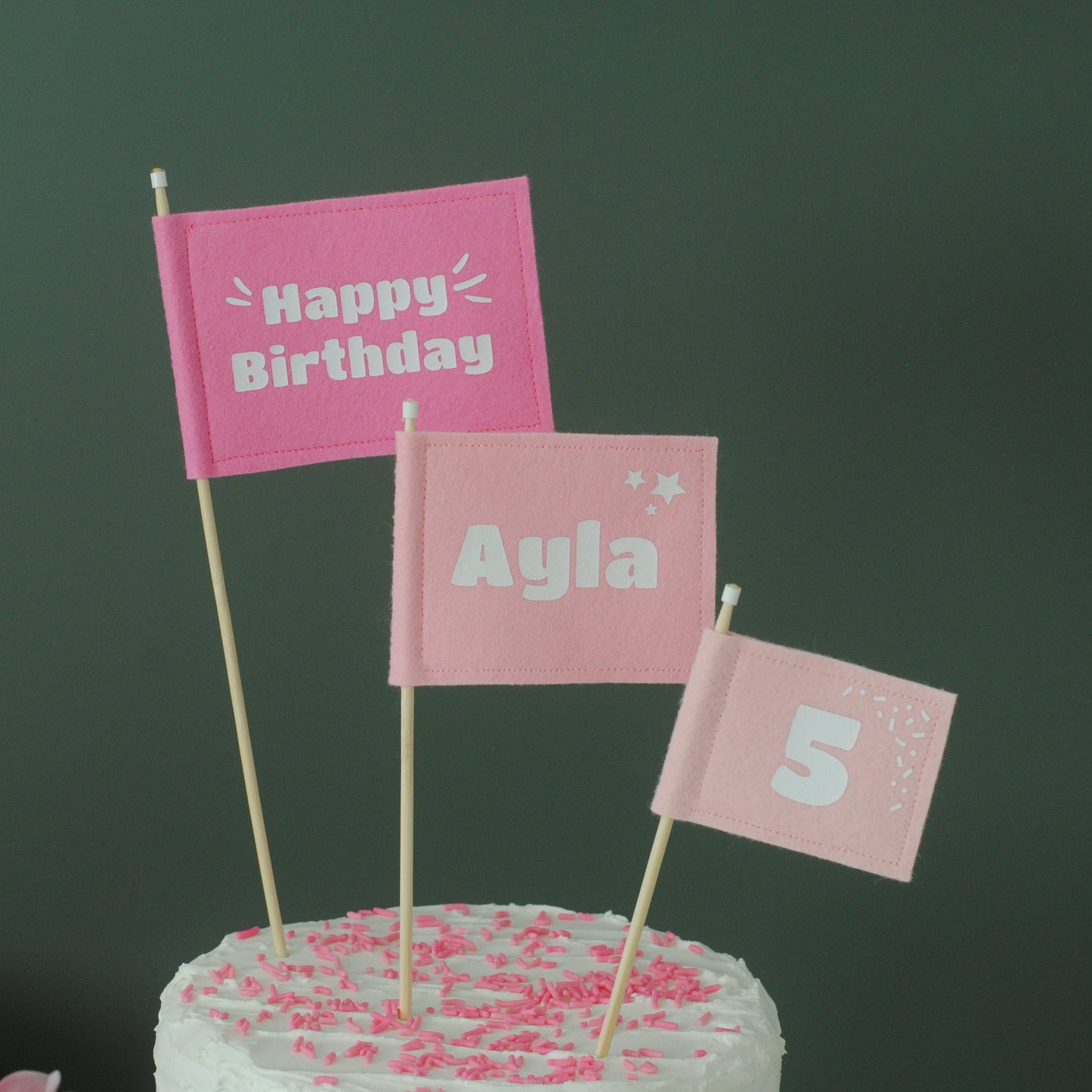 Set of 3 Felt Flag cake topper flags in varying shades of pink.  Big flag has HAPPY BIRTHDAY. Medium flag is personalized with Name: AYLA.  Small flag is personalized with age 5. 