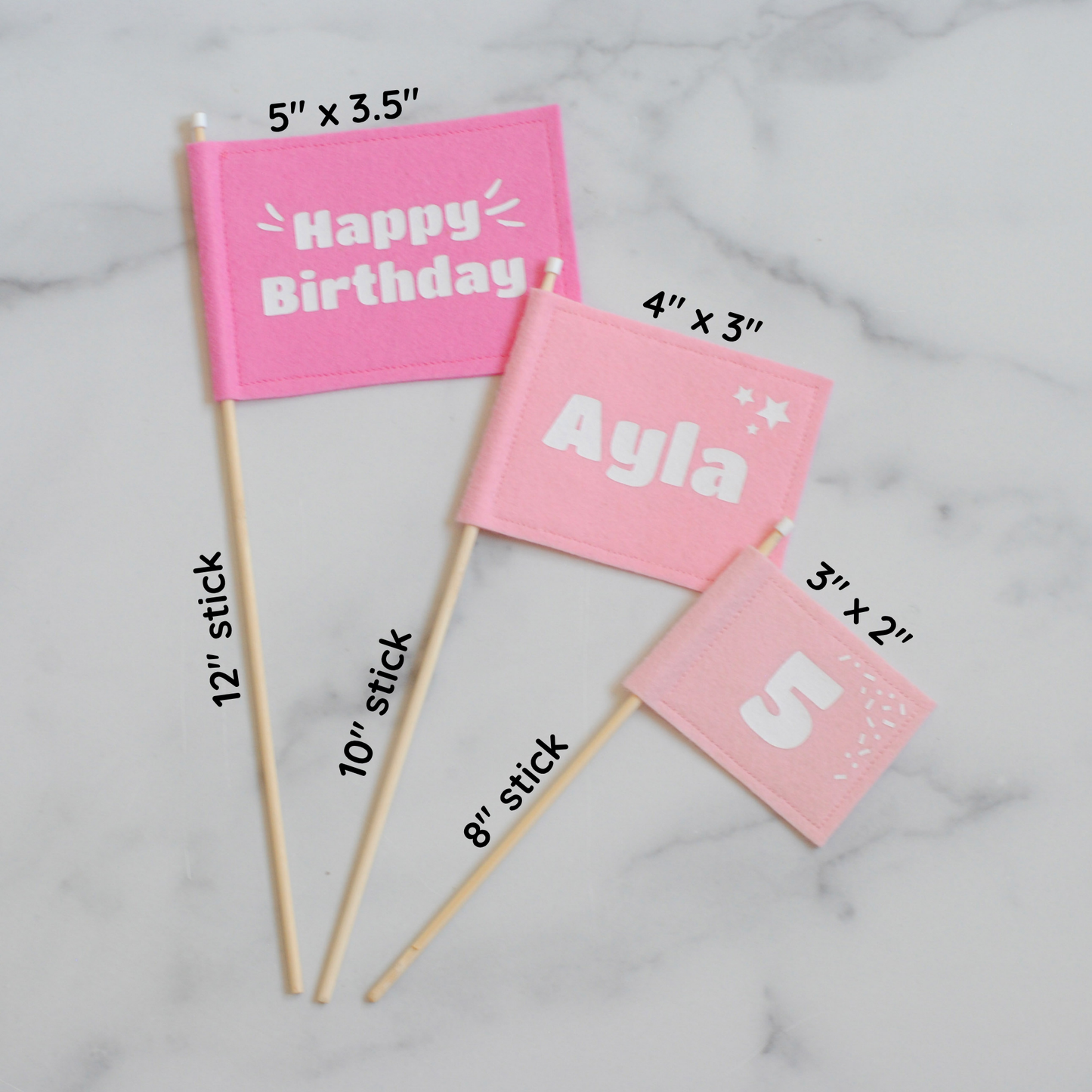 
                  
                    Set of 3 felt flag cake toppers in shades of pink with Happy Birthday, name and age.  Shown flat with flag and stick measurements for each. 
                  
                