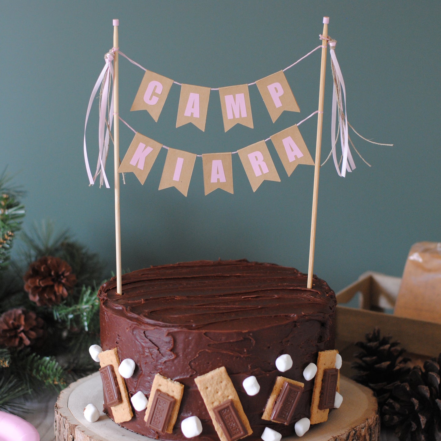 Chocolate cake with s'mores decorations, topped with a 'Camp Kiara' cake topper with pink letters | personalized cake toppers by Avalon Sunshine