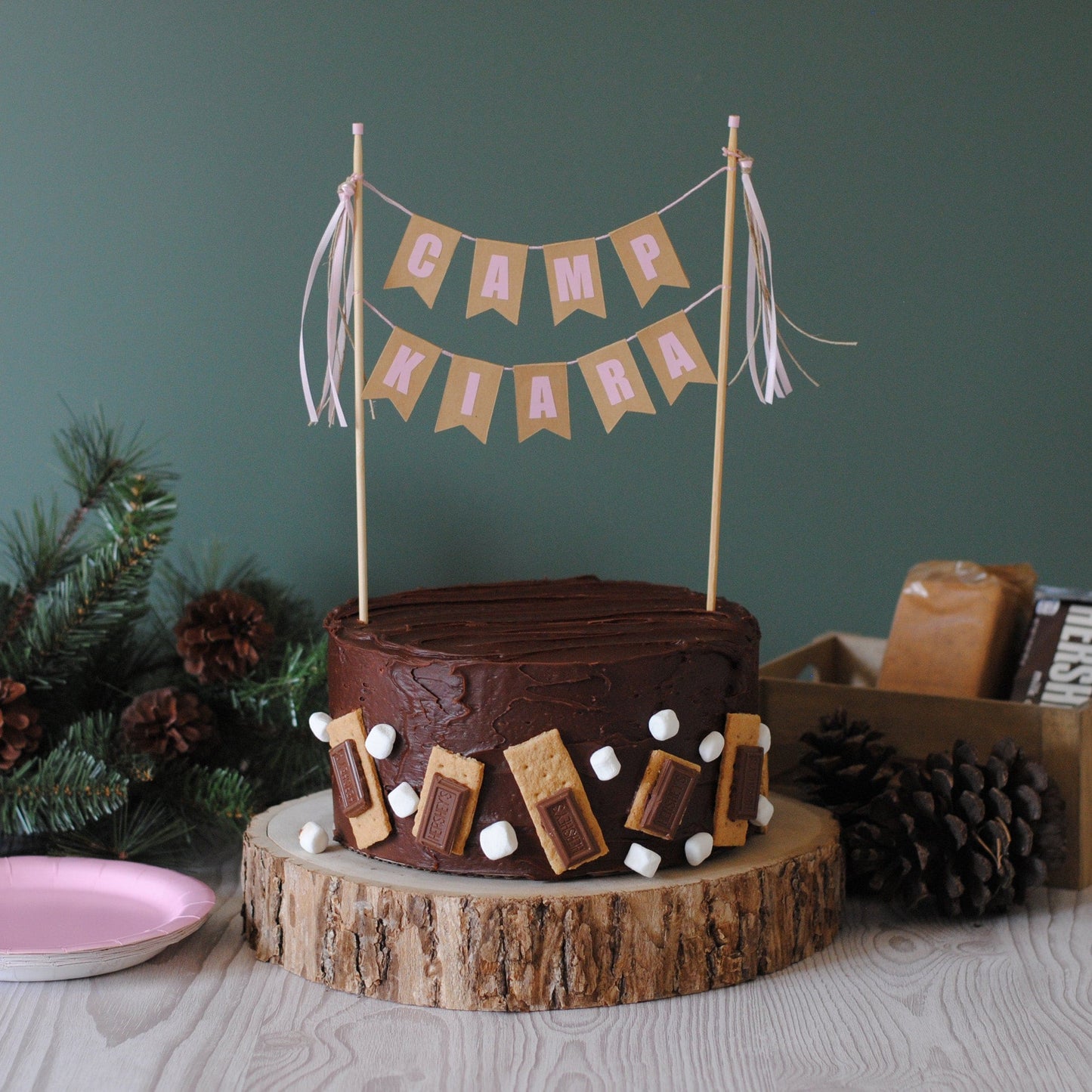 
                  
                    Chocolate cake with s'mores decorations, topped with a 'Camp Kiara' cake topper with pink letters | personalized cake toppers by Avalon Sunshine
                  
                
