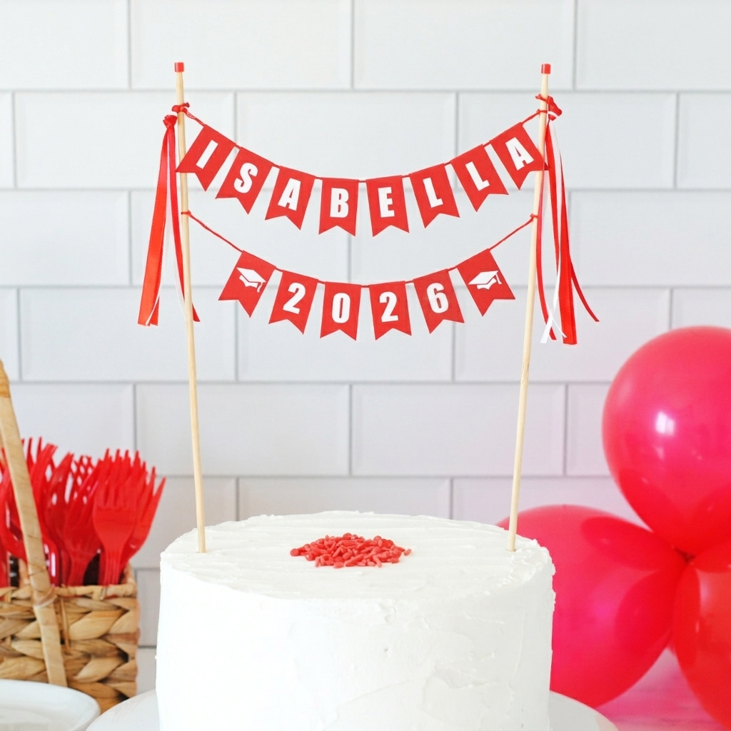 
                  
                    Graduation cake with a 'Isabella 2026' cake banner against a white tiled wall.
                  
                