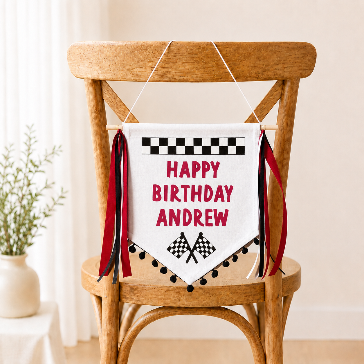 
                  
                    Racing theme irthday banner with 'Happy Birthday Andrew' and checkered flags on a wooden chair
                  
                