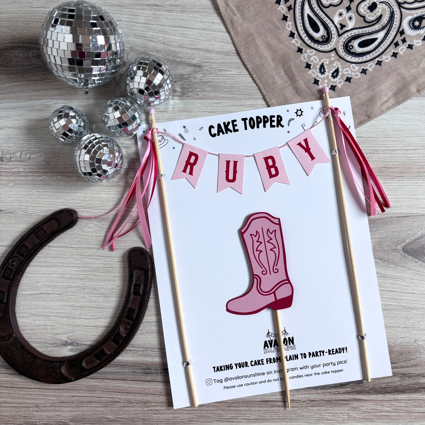 
                  
                    A personalized western cowgirl theme cake topper for a birthday party, displayed in a styled flat-lay with silver disco balls, a horseshoe, and a beige bandana on a light wood background.
                  
                