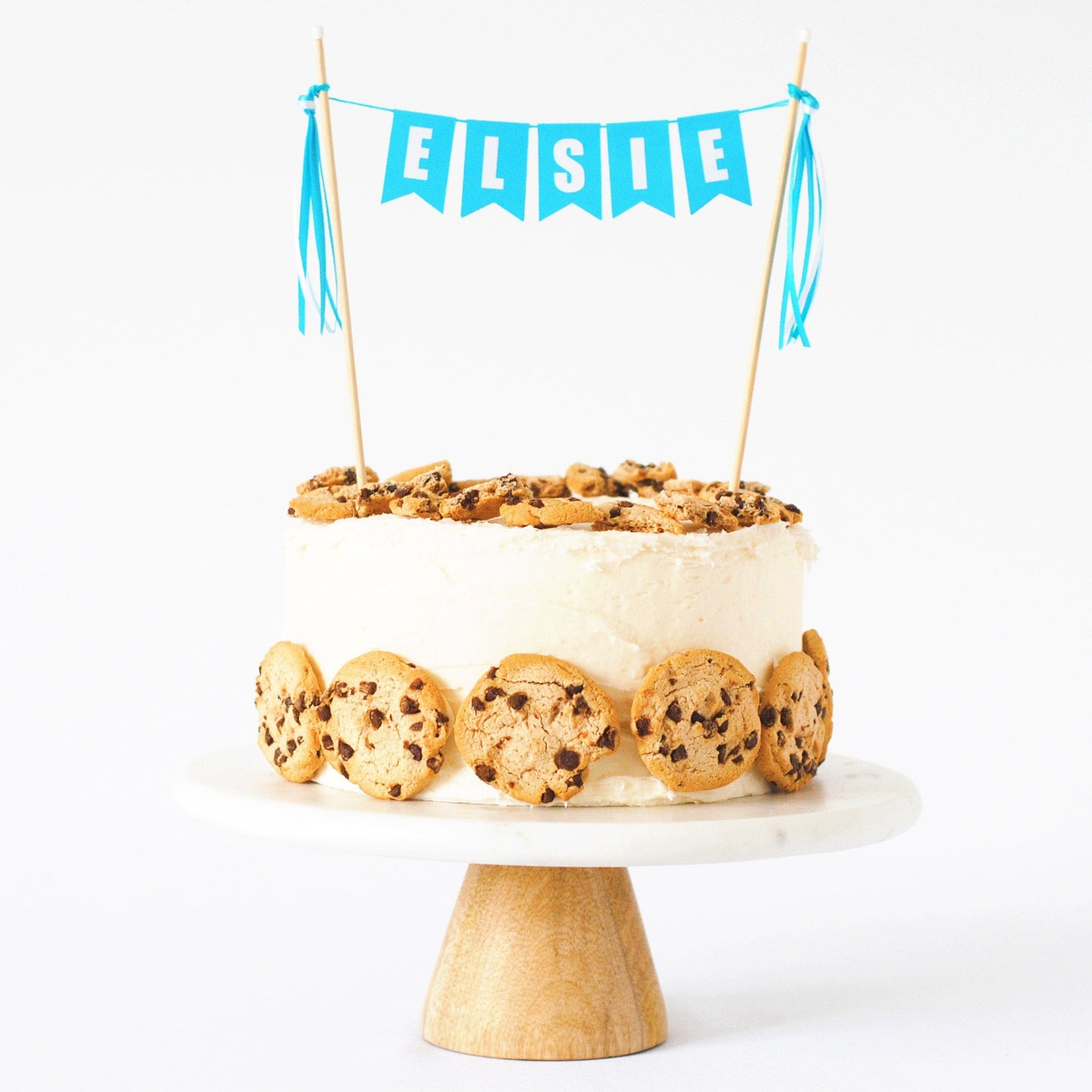 
                  
                    aqua blue cake topper personalized with child's name shown on a white cake decorated with chips ahoy cookies
                  
                