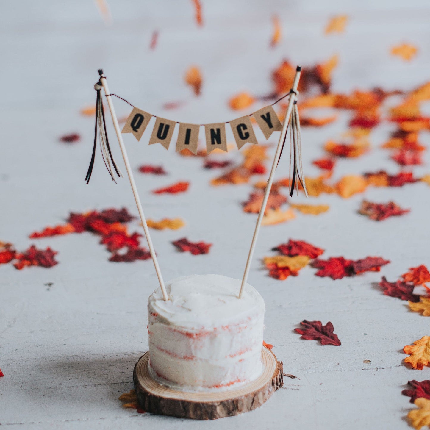 
                  
                    personalized name cake topper shown on small smash cake and fall leaves in the background
                  
                
