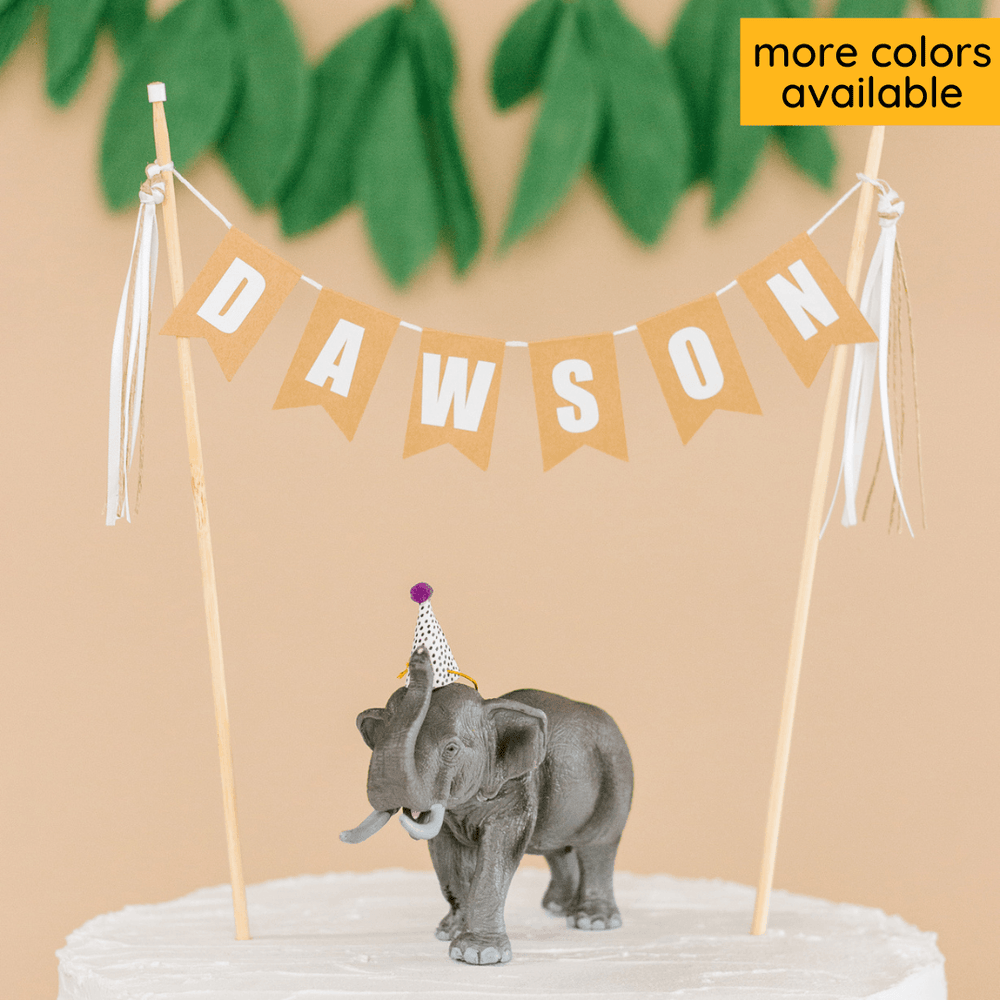 
                  
                    personalized name cake topper for kids birthday cake. neutral colors and an elephant toy on top of the cake
                  
                
