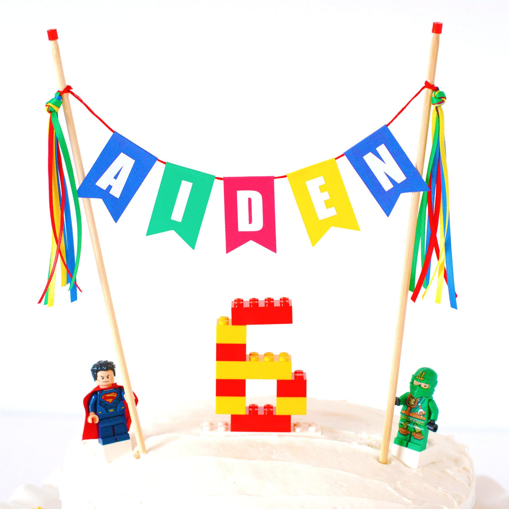 
                  
                    personalized name cake topper shown on a lego birthday cake with lego minifigures
                  
                