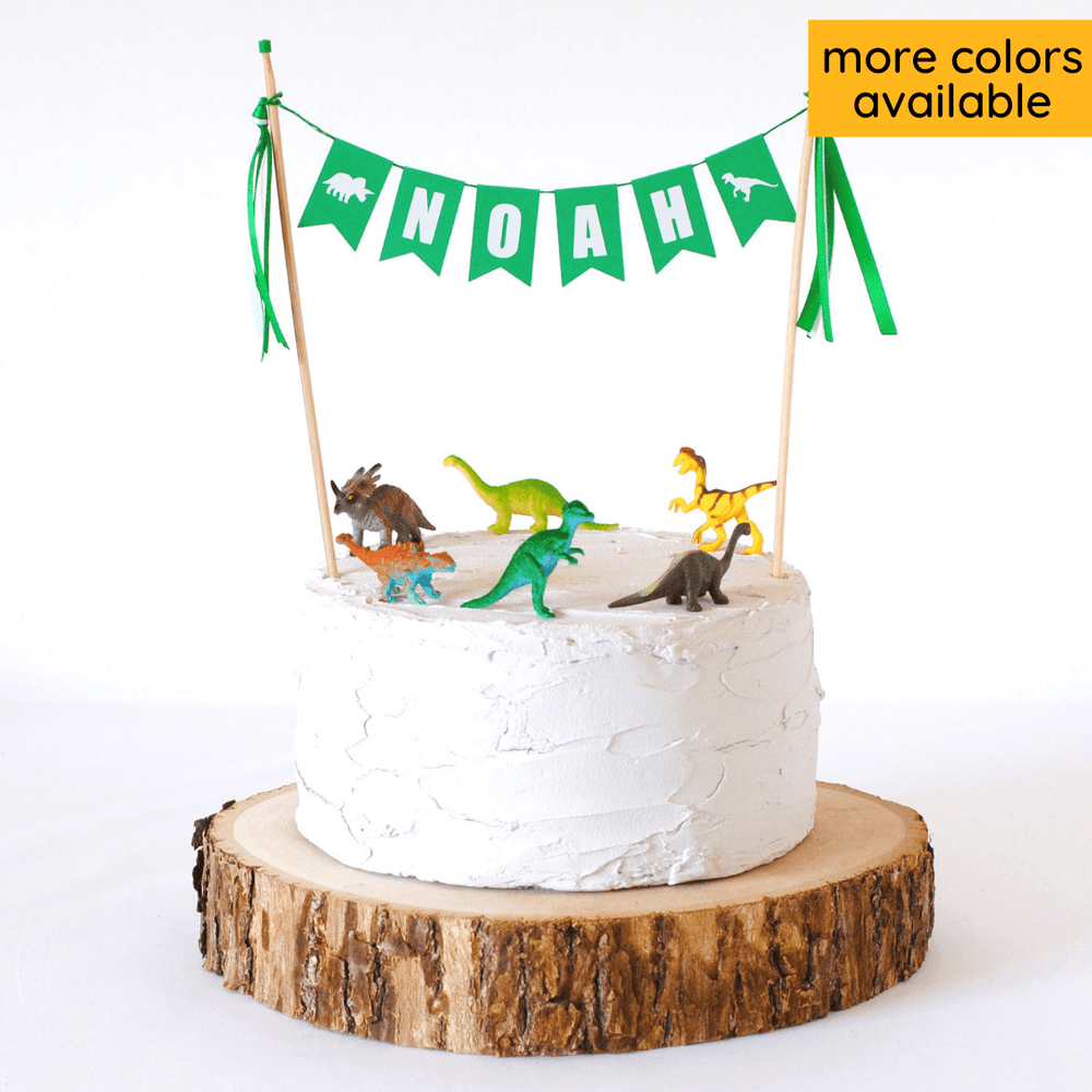 white birthday cake with personalized name banner and mini dinosaur toys on top