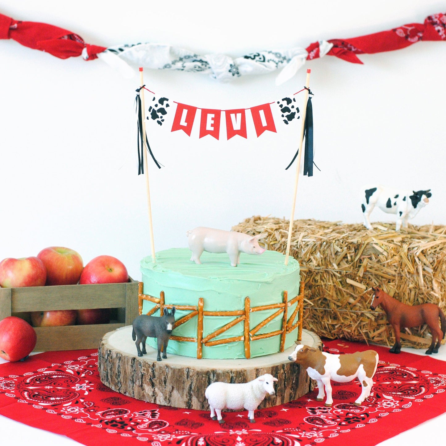 
                  
                    farm birthday party scene with cake and a personalized farm theme cake topper, toy farm animals, hay, apples and a bandana
                  
                