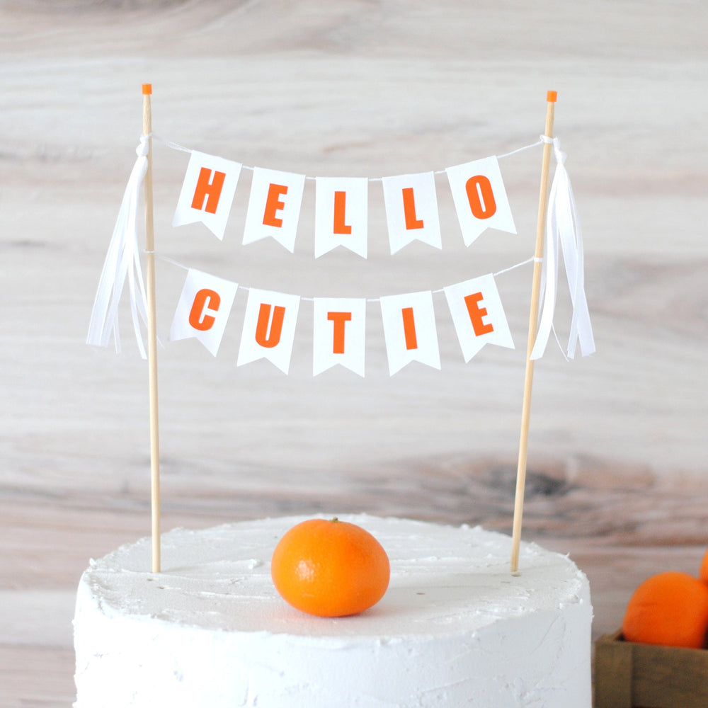 
                  
                    Hello Cutie Cake Topper, white with orange letters and white ribbons
                  
                