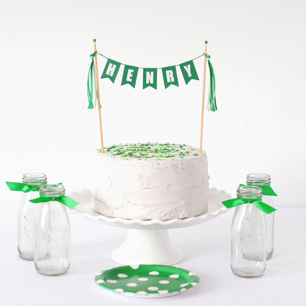 
                  
                    green and white birthday cake topper personalized with child's name on a white cake with sprinkles
                  
                