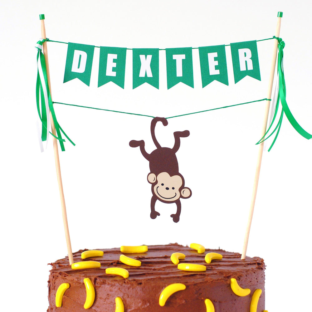 
                  
                    personalized monkey cake topper with name and a monkey hanging from its tail over the cake
                  
                
