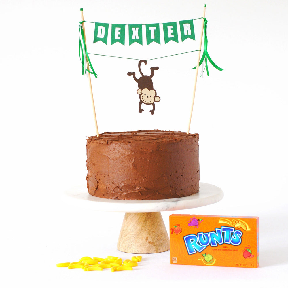 
                  
                    monkey cake topper with name banner and monkey hanging from its tail over chocolate cake and banana runts candy
                  
                