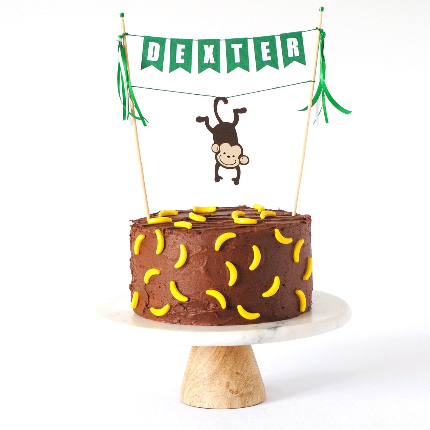 
                  
                    monkey cake topper with personalized name cake banner and monkey hanging from its tail over the cake
                  
                