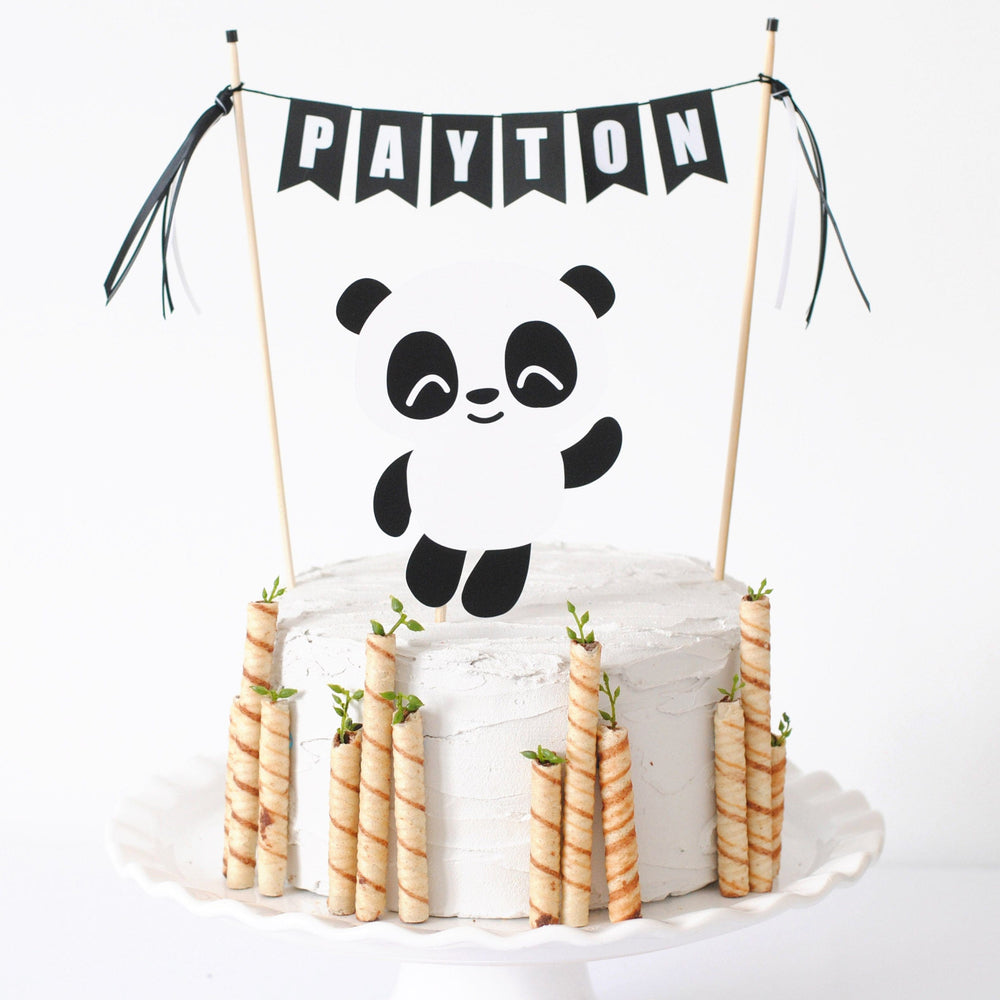 Panda cake topper set with paper panda and a personalized black and white personalized name banner shown on a cake with bamboo cookies