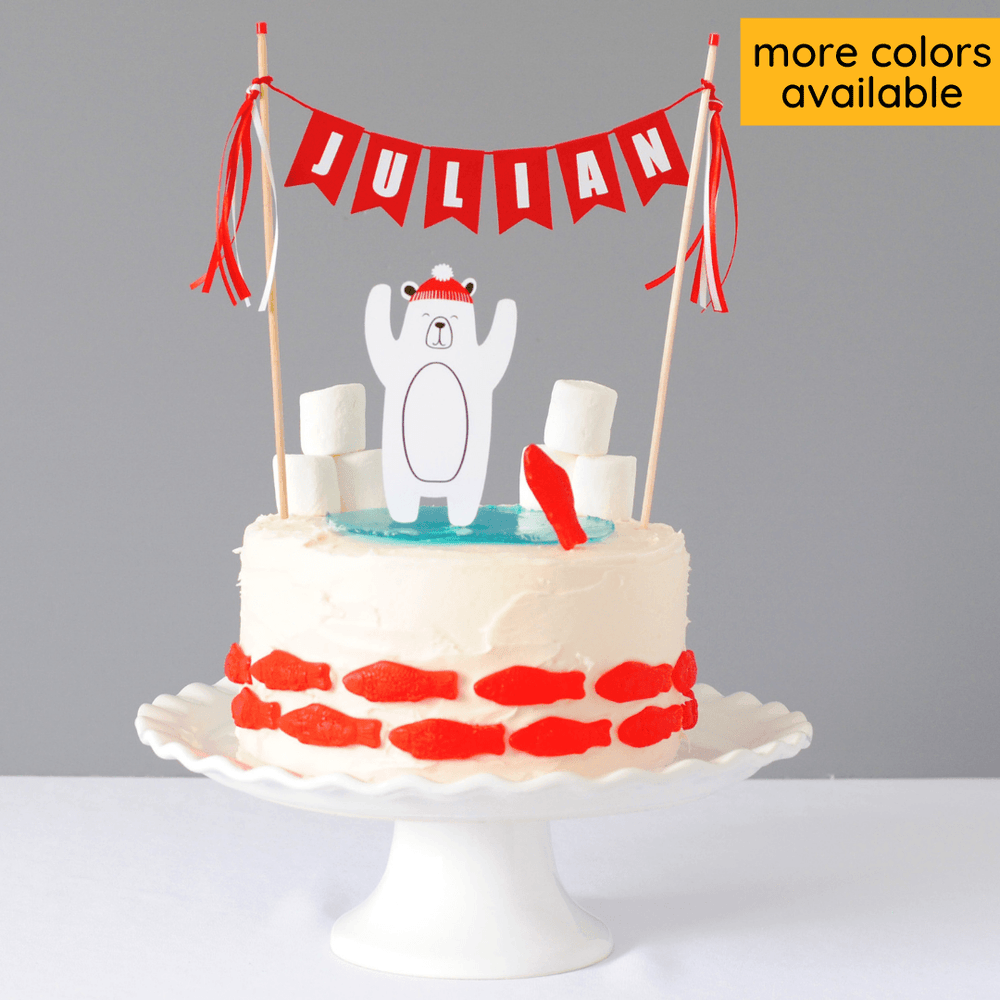 Polar bear birthday cake topper with personalized name banner shown on a white cake with swedish fish and marshmallow snow