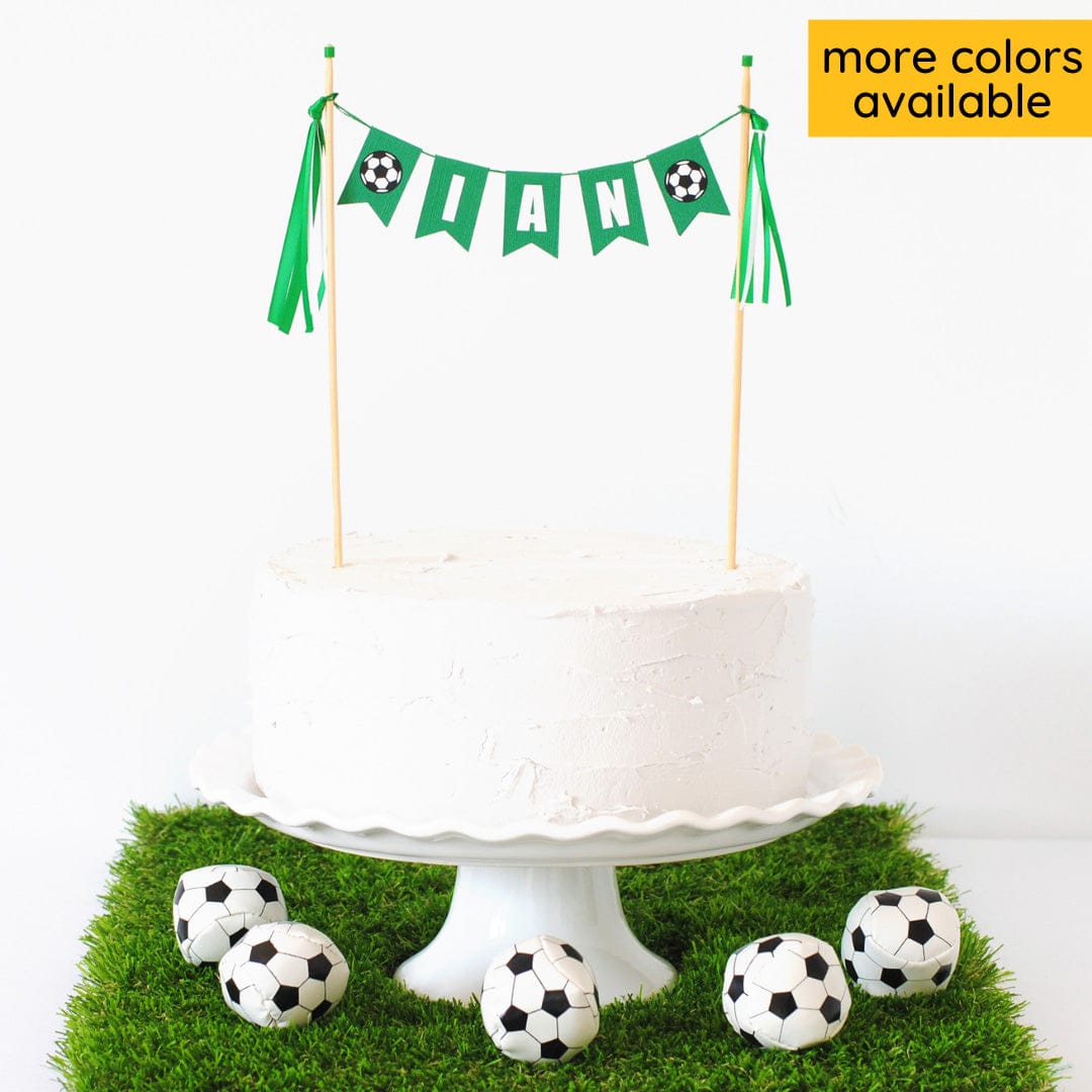 
                  
                    soccer cake topper personalized with child's name with small soccer ball flags on each end made by Avalon Sunshine
                  
                