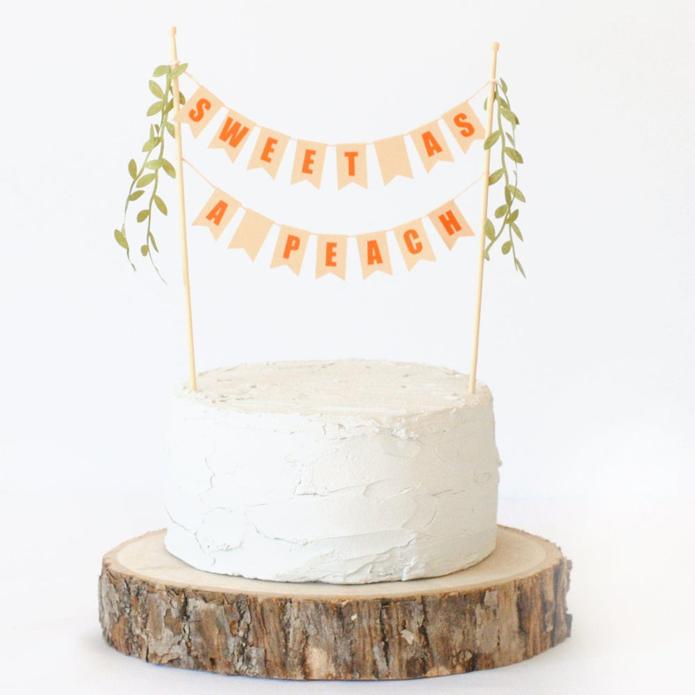 Sweet as a Peach birthday cake topper with mini leaf tassels shown on a wood slice cake stand | Cake topper made by Avalon Sunshine